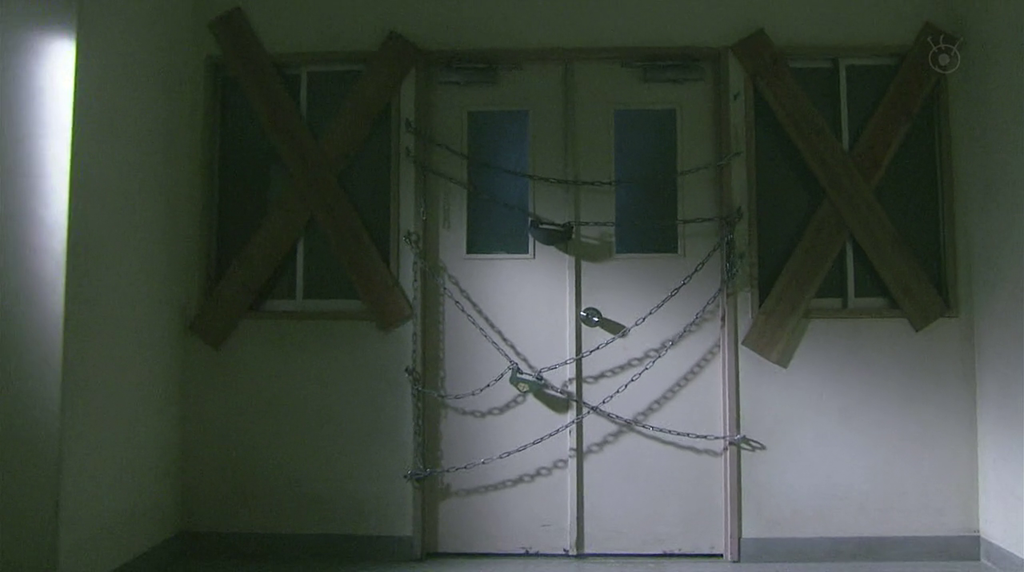 A door flanked by windows at the end of a hallway. Planks are nailed across the windows, and chains are padlocked in fro nt of the doors.